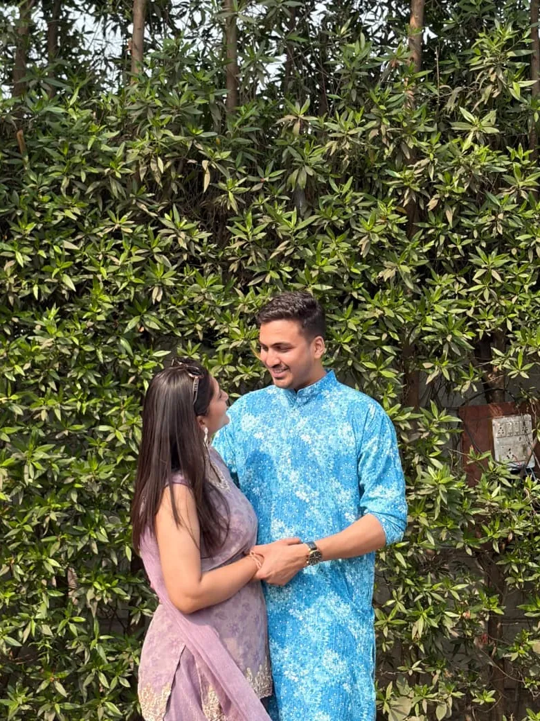 Neha and Sahil holding hands in front of a green hedge